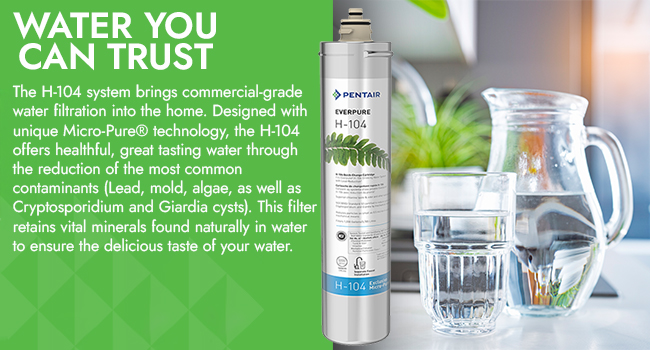Pentair Everpure- H-104 water filter next to a pitcher and a glass of water sitting on a kitchen counter